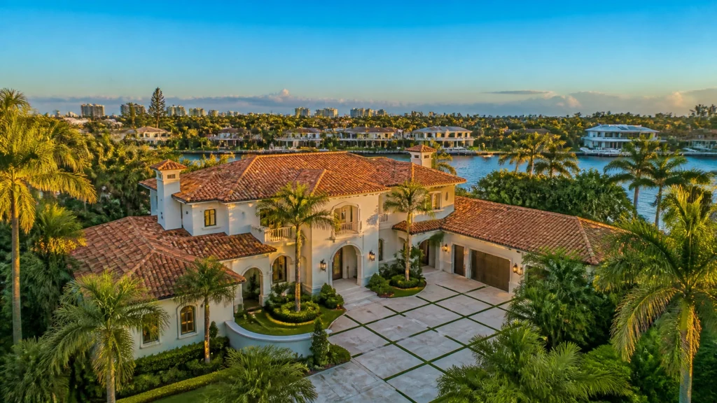 Luxury waterfront home with a clay tile roof and palm-lined driveway in South Florida